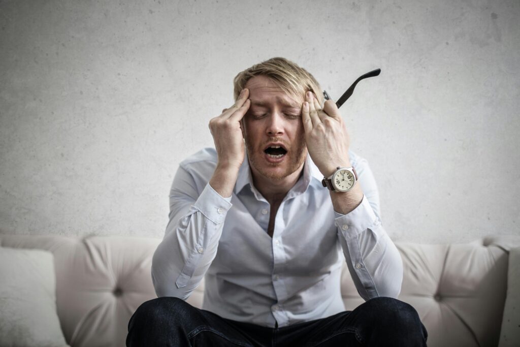 Egy stresszes férfi ül a kanapén a fejét fogva.