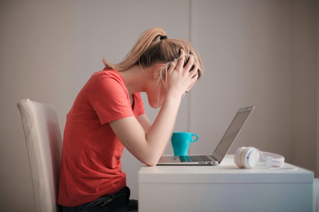Egy stresszes nő ül a laptop előtt a fejét fogva.